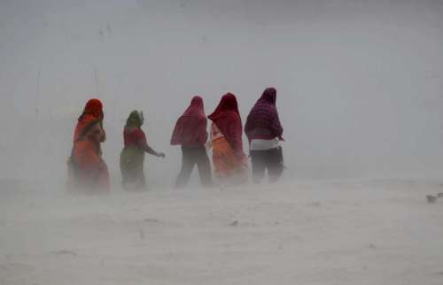 People walk on the banks or river Ganga during a storm in Allahabad, on Oct.13, 2014. (Photo: IANS)