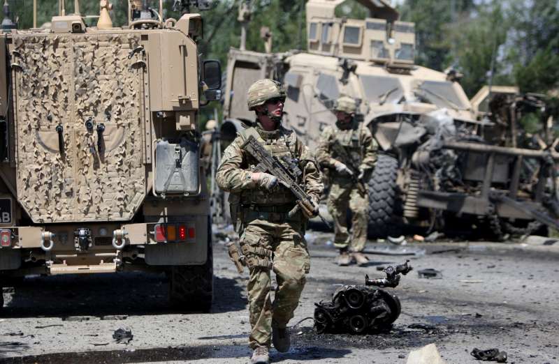 Foreign soldiers walk around a destroyed military vehicle following a suicide car bombing in Kabul, Afghanistan, June 30, 2015. Several civilians were killed and wounded Tuesday after a suicide car bombing targeted a foreign military convoy near airport in Afghan capital of Kabul.