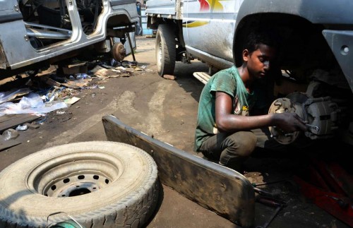 A boy works on a car at a vehicle repair garage 