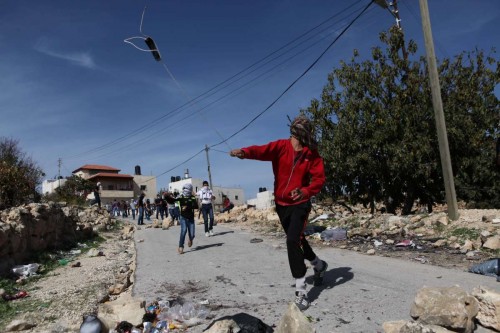 A Palestinian protester hurls stones toward Israeli soldiers during clashes in Jerusalem