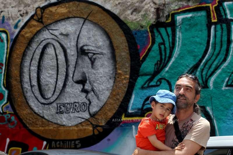 A man and a baby stand before a graffiti on a wall in central Athens, Greece, June 25, 2015. Graffiti artists express the anxiety felt by many Greeks amidst the uncertainty over the ongoing negotiations on the country's debt crisis 