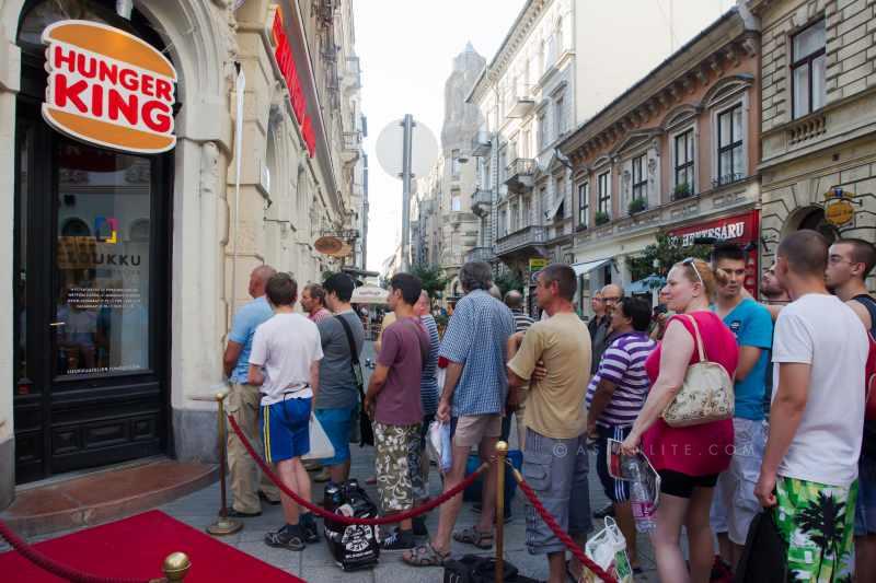 People stand in queue for free money served in hamburger boxes for poor people as part of the Hunger King project by Finnish artist Jani Leinonen in Budapest, Hungary, on June 11, 2014. Jani Leinonen opened a fake takeaway shop with a similar design to Burger King on Wednesday in Budapest. His project aims to raise awareness about poverty in Hungary. Hunger King project offers free money (3400 Hungarian forint, the equivalent of the daily portion of the official minimal wage in Hungary) to poor people willing to stand in queue for hours next to the red carpet offered for rich people in front of the shop