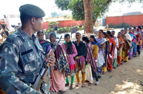  A soldier stands guard at a polling booth as women queue-up to cast their votes during the third phase of Jharkhand assembly polls in Maoist infested Rampur village, near Khijri on Dec 9, 2014. 